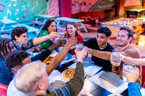 Group of cheerful multi ethnic friends toasting drinks while enjoying a meal together at a bowling