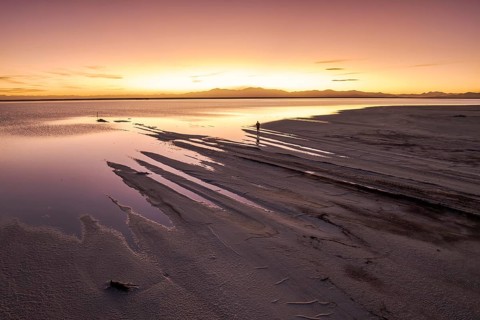 A solo traveler at a mesmerizing sunset in Salinas Grandes, Salta, Argentina, where the vast salt