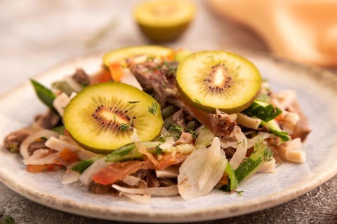 Meat salad with beef kiwi and vegetables on brown concrete background and orange linen textile.