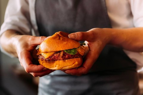 Close-up of an artisan burger presented by a chef. Brioche bun, juicy beef, and melted cheese take