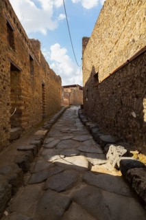 Long narrow street made of large grey smooth and worn lava stones with sidewalk plus remnants of
