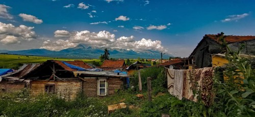 Rural scene with huts and mountains under a wide cloudy sky, atmospheric atmosphere, bright colors,