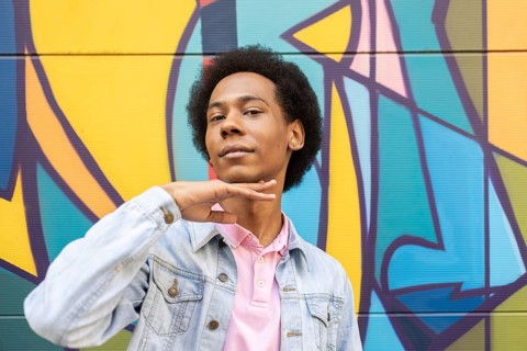 A confident non-binary person stands proudly in front of a vibrant graffiti mural. They wear a