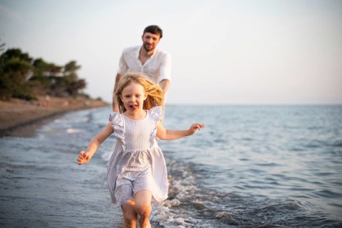 A young girl runs barefoot through the shallow waves of an Italian beach, smiling with joy as her
