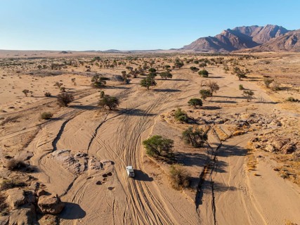 Aerial view of off-road car driving in dry riverbed and desert landscape on the Ugab River, behind