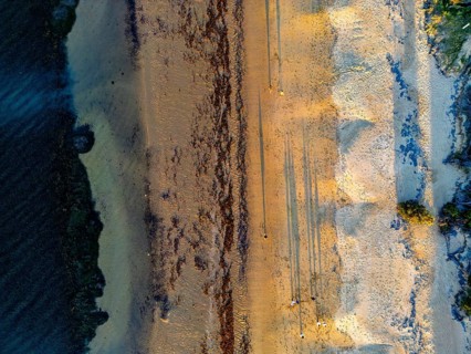 Aerial shot of a sandy beach during sunset, casting long shadows across the sand in the Great Ocean
