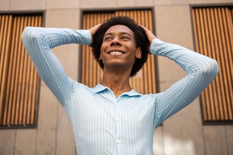 A joyful non-binary individual confidently poses outdoors in a vibrant urban setting, showcasing a