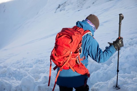 A skier with a red backpack explores a winter landscape during a ski touring adventure. The