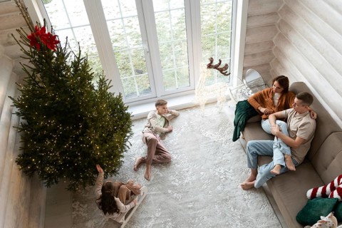 A family celebrates Christmas in a cozy room adorned with a large, lit Christmas tree. A couple