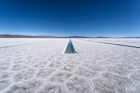 Endless white salt crust of Salinas Grandes and pool channels under a clear blue sky, with distant