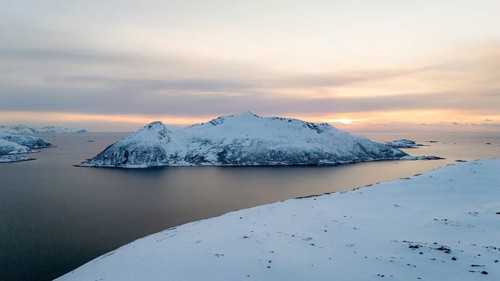 A breathtaking aerial view captures a Nordic winter landscape with a tranquil snowy island