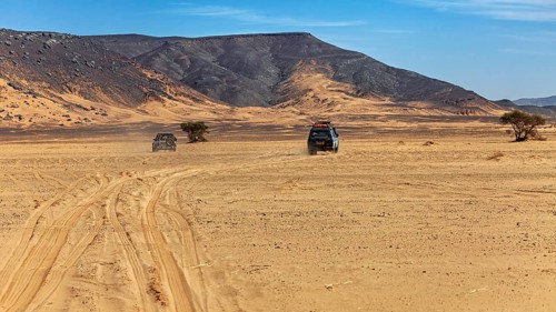 Two vehicles leave tracks on a large, flat expanse of sand near the mountains, With off-road