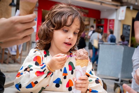 A young girl delights in eating chocolate ice cream from a cone in a quaint village scene,