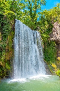 A waterfall is flowing into a pool of water. The water is clear and the sky is blue