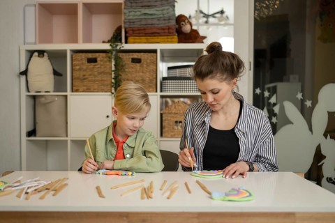 A teacher guides a child through a fun art lesson. The room is filled with colorful supplies,