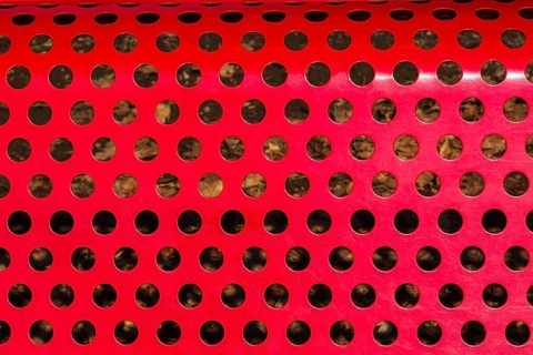 Close-up of vibrant red painted metal sitting bench backrest with perforated round holes, Quebec,