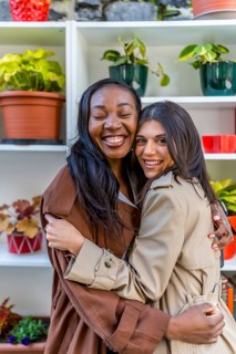 Two multi ethnic female friends are hugging each other with eyes closed in a plant shop,