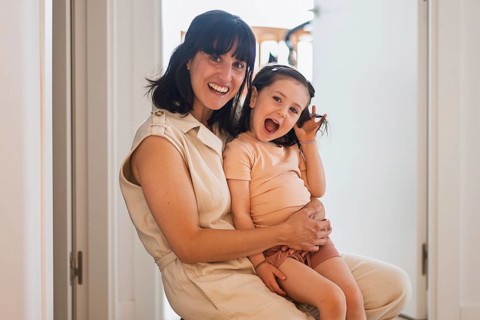 A joyful young mother lovingly embraces her playful toddler daughter in a bright home environment.
