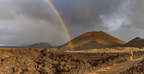 A vibrant rainbow arcs over the rugged volcanic terrain of Timanfaya National Park in Lanzarote,