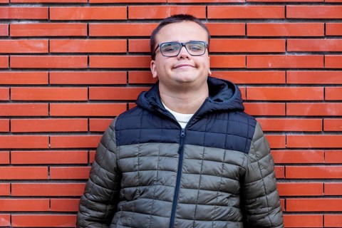Man with an intellectual disability smiles warmly while leaning against a brick wall. His relaxed