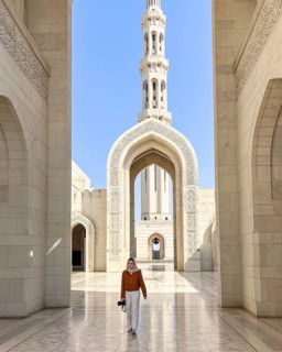 A woman wearing an headscarf walks through the grand architecture of the Sultan Qaboos Mosque in
