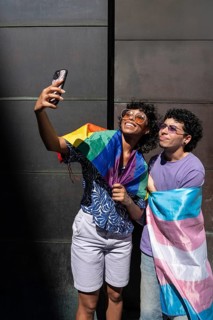 A joyful multiethnic LGBTQ+ couple takes a selfie wrapped in pride flags, celebrating love,