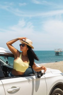 A young Latin woman in a yellow top and sunglasses enjoying the breeze and ocean view from a car at
