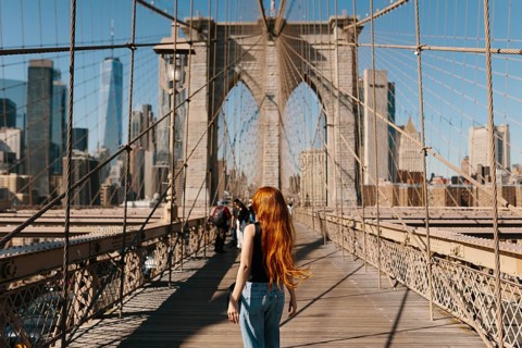 A woman with long hair walks on the iconic Brooklyn Bridge in New York City, capturing the stunning