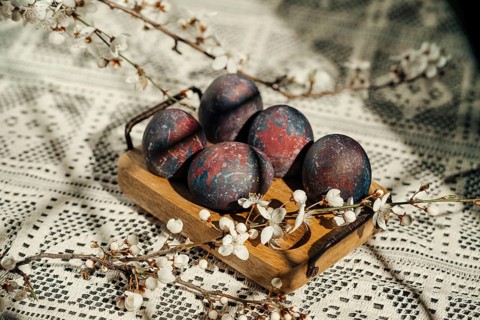 Cosmic-painted Easter eggs displayed on a rustic wooden tray, adorned with delicate white spring