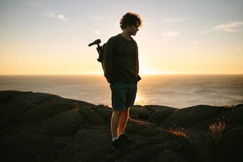 A young male photographer stands on the rocky terrain of Cape Spear Lighthouse, Newfoundland &