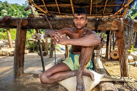 A young man sits relaxed in a rustic outdoor wooden structure, the sapphire and gemstone mines at