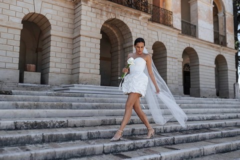 A beautiful bride in a white dress and veil gracefully descends the ancient stone steps of a