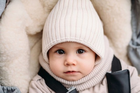 A young child in cozy autumn attire gazes with curiosity. The child wears a knitted hat and