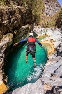 A canyoneer leaps into vibrant turquoise waters surrounded by rugged cliffs in Matacanes, Nuevo