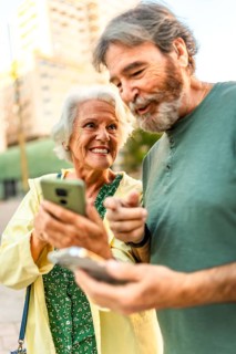 Vertical close-up of a happy senior couple walking using mobile phone in the city