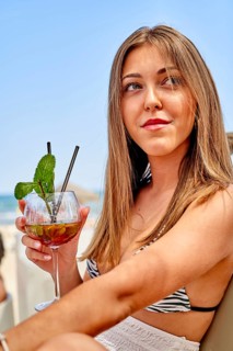 A young woman relaxes at the beach, enjoying a colorful cocktail while soaking up the sun. The