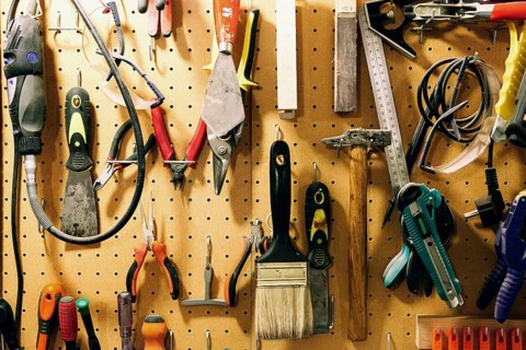 Pegboard displaying assorted luthier tools for crafting bass guitars, including pliers, brushes,