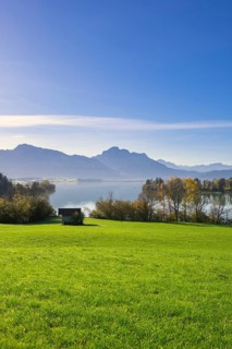 Landscape with lake, grassy meadow and mountains in the background, under a clear blue sky, wooden