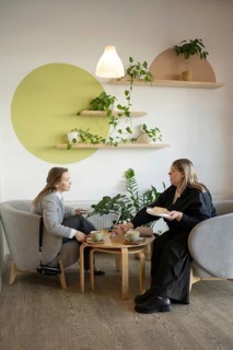 Two women enjoy a friendly chat over coffee in a cozy, stylish cafe with modern decor and lush