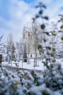 Snow-covered church with decorated tower behind trees and bushes, Aidlingen, Böblingen district,