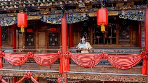 A woman in traditional Qing Dynasty attire stands on a beautifully decorated balcony in Pingyao,