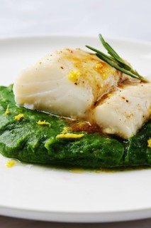 A succulent cod fillet sits atop a beautiful green spinach puree, garnished with herbs and citrus
