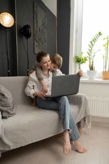 A mother working on a laptop at home with her young child lovingly embracing her. A cozy, modern