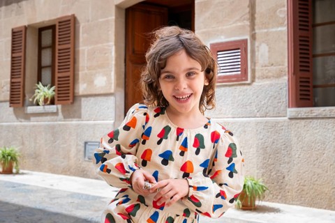 A joyful child, dressed in colorful attire, plays in the sunlit street of a quaint village,