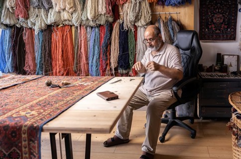 An Iranian master craftsman meticulously restores a carpet in his well-organized workshop in