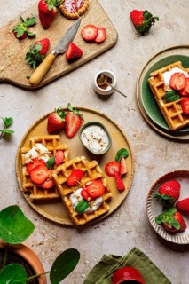 Rustic homemade waffles topped with fresh strawberries, yoghurt, and mint. Served on ceramic