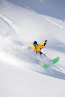 A snowboarder in a vibrant yellow jacket expertly carves through fresh powder on a snowy mountain