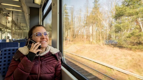 A woman in a cozy jacket is talking on her phone while traveling on a train. She gazes happily out