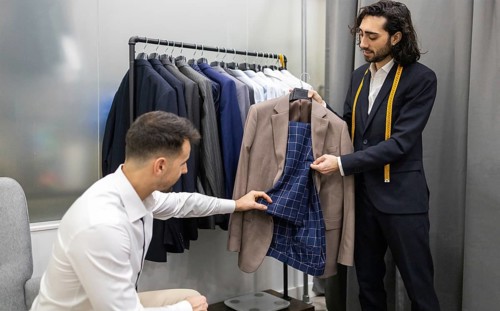 A tailor assists a customer in selecting a suit in modern store. The tailor shows the inner lining