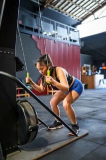 Vertical photo of a Chinese strong woman bending while pulling weights with a lat machine in a